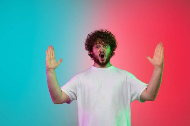 Beyaz tenli genç adam, neon renkli gradyan stüdyo arka planında portre çiziyor.