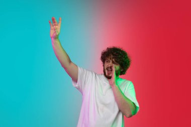 Beyaz tenli genç adam, neon renkli gradyan stüdyo arka planında portre çiziyor.