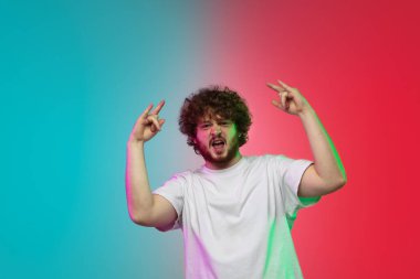 Beyaz tenli genç adam, neon renkli gradyan stüdyo arka planında portre çiziyor.