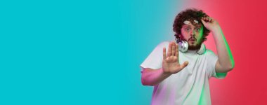 Beyaz tenli genç adam, neon renkli gradyan stüdyo arka planında portre çiziyor.