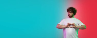 Beyaz tenli genç adam, neon renkli gradyan stüdyo arka planında portre çiziyor.