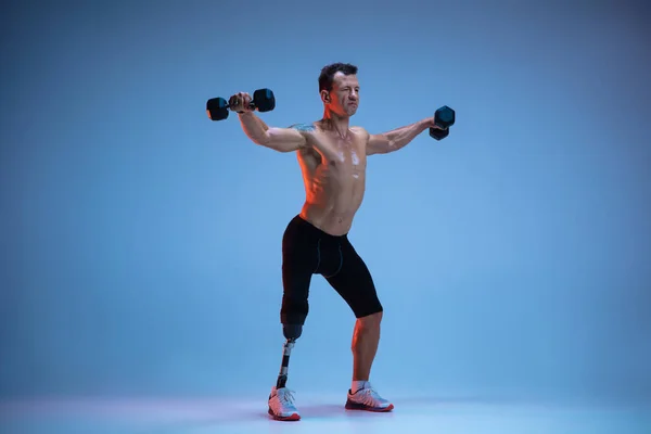 Atleta con discapacidad o amputado aislado en el fondo del estudio azul. Deportista masculino profesional con entrenamiento de prótesis de pierna con pesas en neón — Foto de Stock