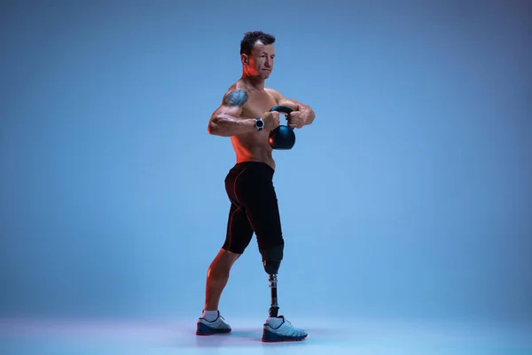 Atleta con discapacidad o amputado aislado en el fondo del estudio azul. Deportista masculino profesional con entrenamiento de prótesis de pierna con pesas en neón — Foto de Stock