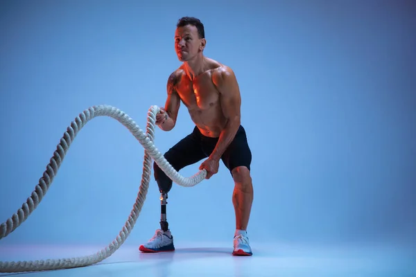 Atleta con discapacidad o amputado aislado en el fondo del estudio azul. Deportista masculino profesional con entrenamiento de prótesis de pierna con pesas en neón — Foto de Stock