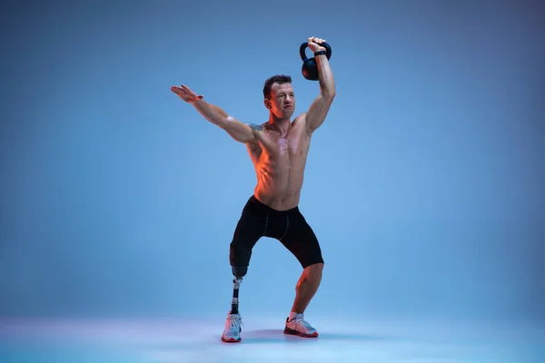 Atleta con discapacidad o amputado aislado en el fondo del estudio azul. Deportista masculino profesional con entrenamiento de prótesis de pierna con pesas en neón — Foto de Stock