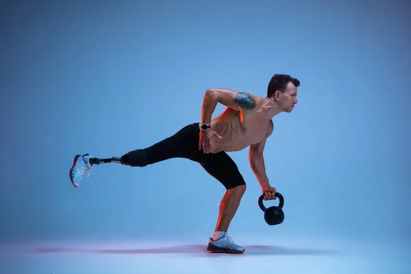 Atleta con discapacidad o amputado aislado en el fondo del estudio azul. Deportista masculino profesional con entrenamiento de prótesis de pierna con pesas en neón — Foto de Stock