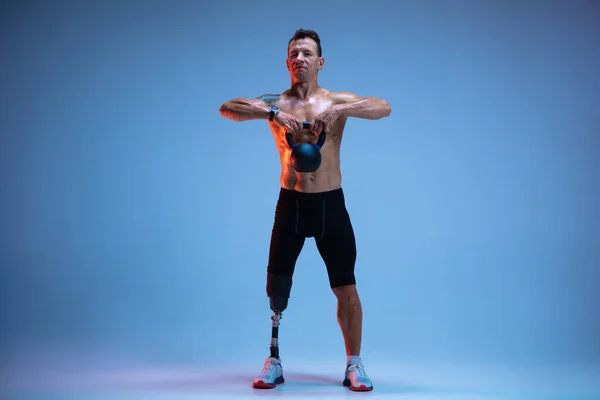 Atleta con discapacidad o amputado aislado en el fondo del estudio azul. Deportista masculino profesional con entrenamiento de prótesis de pierna con pesas en neón — Foto de Stock