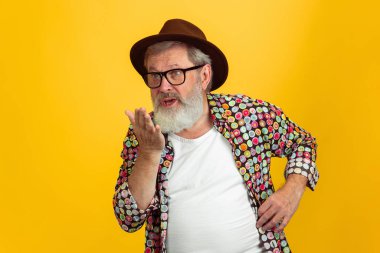 Kıdemli hippi gözlüklü adam sarı arka planda poz veriyor. Teknolojik ve neşeli yaşlı yaşam tarzı konsepti