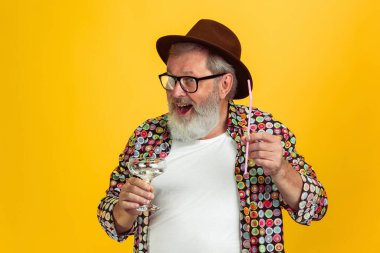 Kıdemli hippi gözlüklü adam sarı arka planda poz veriyor. Teknolojik ve neşeli yaşlı yaşam tarzı konsepti