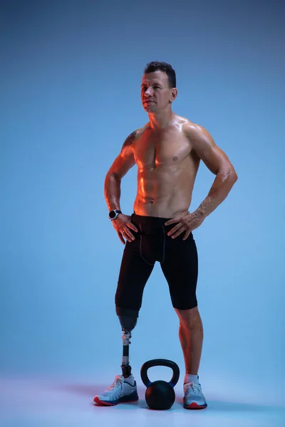 Atleta con discapacidad o amputado aislado en el fondo del estudio azul. Deportista masculino profesional con entrenamiento de prótesis de pierna con pesas en neón — Foto de Stock