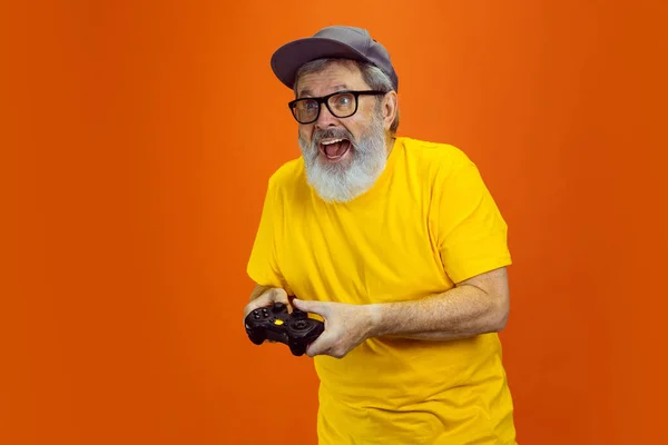 Hombre hipster senior usando dispositivos, artilugios sobre fondo naranja. Tecnología y alegre concepto de estilo de vida de ancianos — Foto de Stock