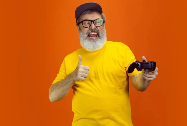 Hombre hipster senior usando dispositivos, artilugios sobre fondo naranja. Tecnología y alegre concepto de estilo de vida de ancianos — Foto de Stock