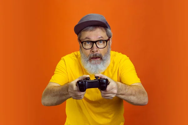 Hombre hipster senior usando dispositivos, artilugios sobre fondo naranja. Tecnología y alegre concepto de estilo de vida de ancianos — Foto de Stock