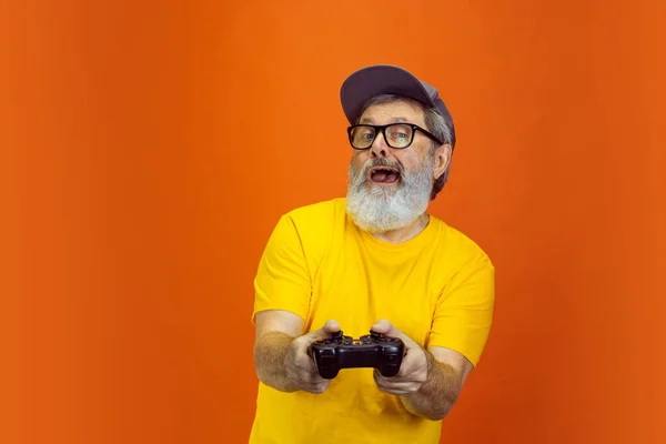 Senior hipster man met behulp van apparaten, gadgets op oranje achtergrond. Technisch en vrolijk ouderenlevensstijl concept — Stockfoto