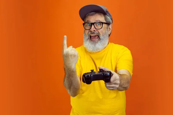 Hombre hipster senior usando dispositivos, artilugios sobre fondo naranja. Tecnología y alegre concepto de estilo de vida de ancianos — Foto de Stock