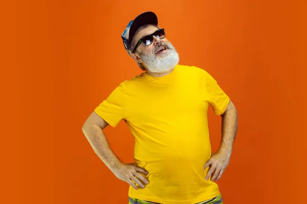 Kıdemli hippi gözlüklü adam turuncu arka planda poz veriyor. Teknolojik ve neşeli yaşlı yaşam tarzı konsepti — Stok fotoğraf