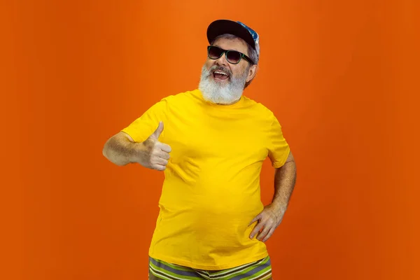 Hombre hipster senior con anteojos posando sobre fondo naranja. Tecnología y alegre concepto de estilo de vida de ancianos — Foto de Stock