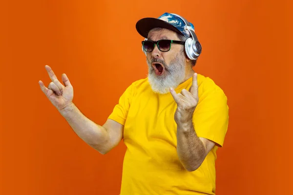 Senior hipster man met behulp van apparaten, gadgets op oranje achtergrond. Technisch en vrolijk ouderenlevensstijl concept — Stockfoto