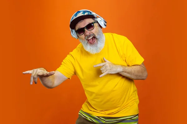 Hombre hipster senior usando dispositivos, artilugios sobre fondo naranja. Tecnología y alegre concepto de estilo de vida de ancianos — Foto de Stock