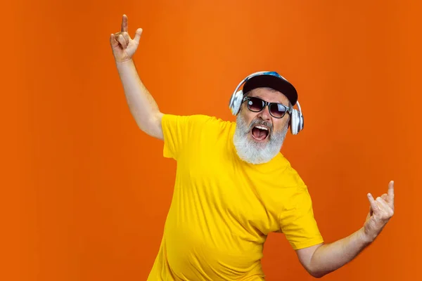 Uomo hipster anziano che usa dispositivi, gadget su sfondo arancione. Tecnologia e gioioso stile di vita anziano concetto — Foto Stock