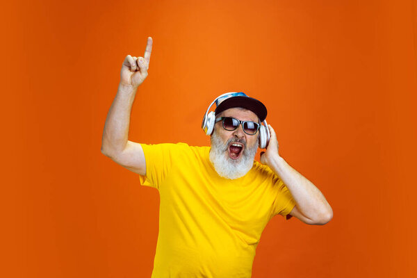 Старший хипстер использует устройства, гаджеты на оранжевом фоне. Технология и радостный образ жизни пожилых людей