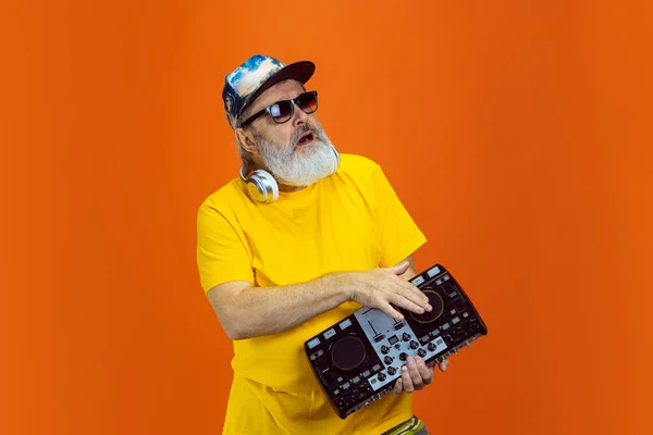 Senior hipster man using devices, gadgets on orange background. Tech and joyful elderly lifestyle concept — Stock Photo, Image