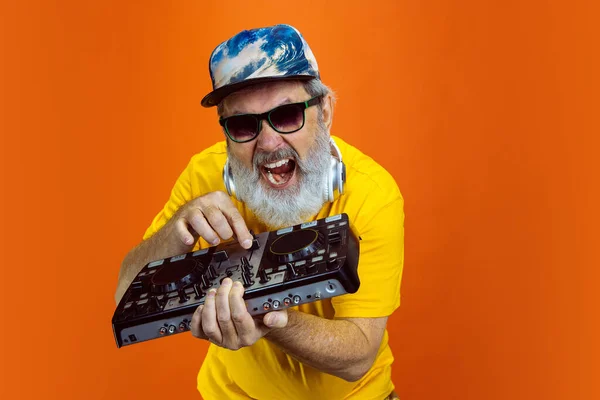 Hombre hipster senior usando dispositivos, artilugios sobre fondo naranja. Tecnología y alegre concepto de estilo de vida de ancianos — Foto de Stock