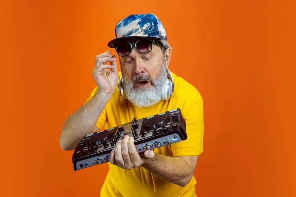 Starší hipster muž pomocí zařízení, gadgets na oranžové pozadí. Technický a radostný životní styl seniorů — Stock fotografie