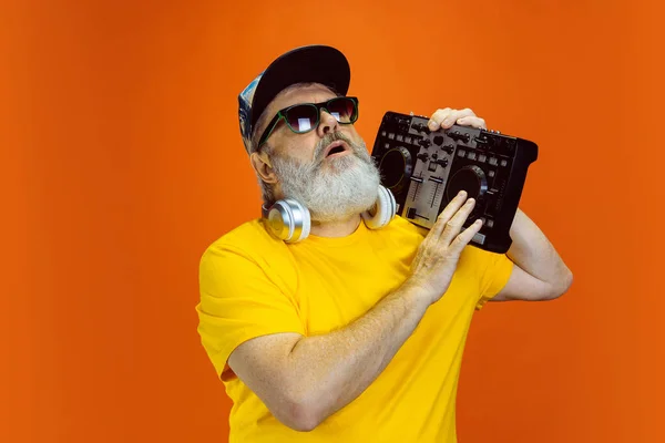 Hombre hipster senior usando dispositivos, artilugios sobre fondo naranja. Tecnología y alegre concepto de estilo de vida de ancianos — Foto de Stock