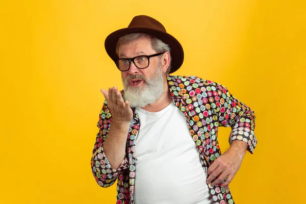 Kıdemli hippi gözlüklü adam sarı arka planda poz veriyor. Teknolojik ve neşeli yaşlı yaşam tarzı konsepti