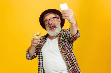 Kıdemli hippi gözlüklü adam sarı arka planda poz veriyor. Teknolojik ve neşeli yaşlı yaşam tarzı konsepti