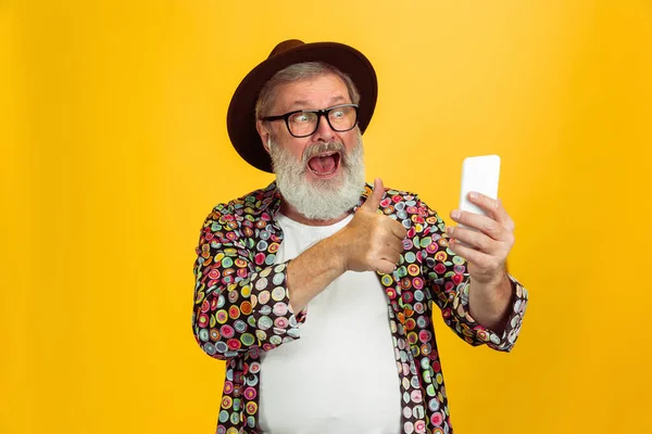 Homem hipster sênior usando óculos posando no fundo amarelo. Conceito de tecnologia e estilo de vida idoso alegre — Fotografia de Stock