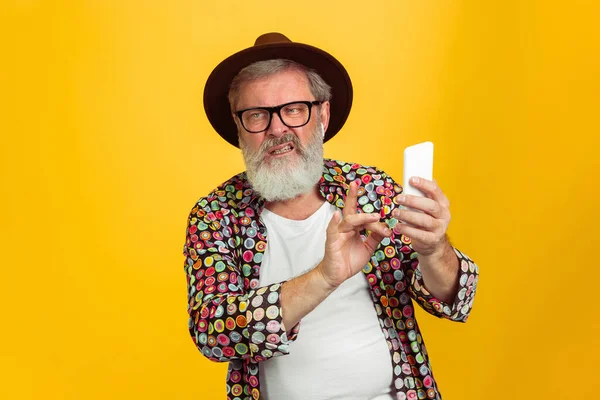 Homem hipster sênior usando óculos posando no fundo amarelo. Conceito de tecnologia e estilo de vida idoso alegre — Fotografia de Stock