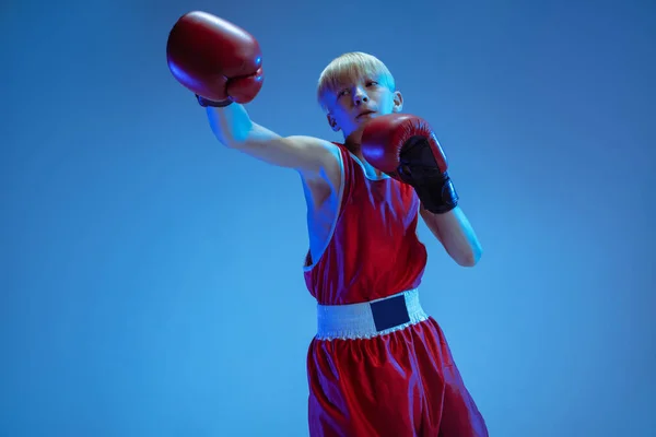 Adolescente em sportswear boxe isolado no fundo do estúdio azul em luz de néon — Fotografia de Stock