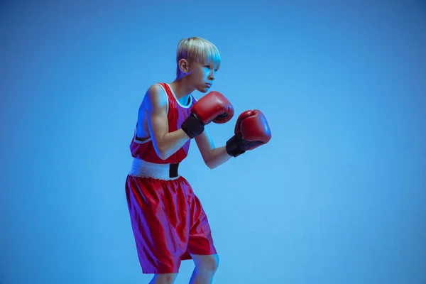 Adolescente em sportswear boxe isolado no fundo do estúdio azul em luz de néon — Fotografia de Stock