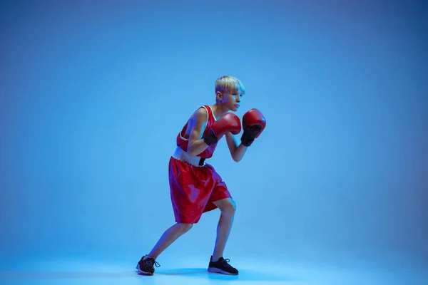 Adolescente en el boxeo de ropa deportiva aislado en fondo de estudio azul en luz de neón —  Fotos de Stock