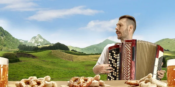 The happy smiling man with beer dressed in traditional Austrian or Bavarian costume holding mug of beer, mountains on background, flyer — Stock Photo, Image