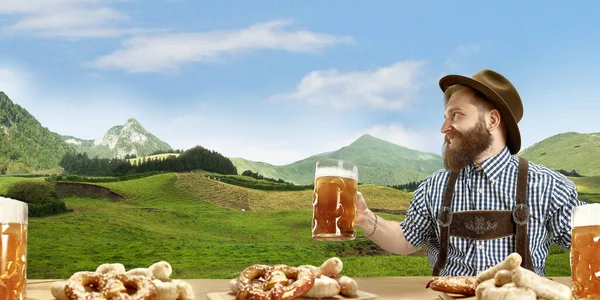 The happy smiling man with beer dressed in traditional Austrian or Bavarian costume holding mug of beer, mountains on background, flyer — Stock Photo, Image