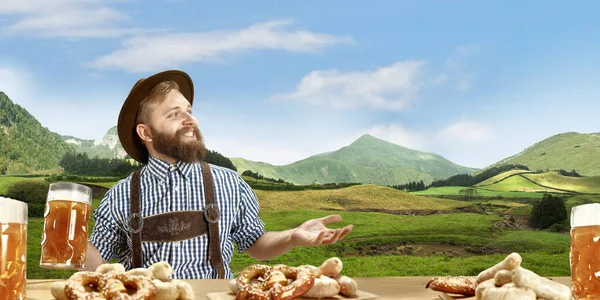 El hombre sonriente feliz con cerveza vestida con traje tradicional austriaco o bávaro sosteniendo taza de cerveza, montañas en el fondo, volante — Foto de Stock