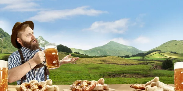 A vidám, mosolygós férfi hagyományos osztrák vagy bajor jelmezbe öltözött sörrel, kezében korsó sörrel, hegyek a háttérben, szórólap — Stock Fotó