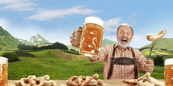 El anciano feliz sonriente hombre con cerveza vestida con traje tradicional austriaco o bávaro sosteniendo taza de cerveza, montañas en el fondo, volante —  Fotos de Stock
