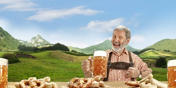 The senior happy smiling man with beer dressed in traditional Austrian or Bavarian costume holding mug of beer, mountains on background, flyer — Stock Photo, Image