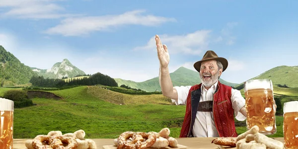 The senior happy smiling man with beer dressed in traditional Austrian or Bavarian costume holding mug of beer, mountains on background, flyer — Stock Photo, Image