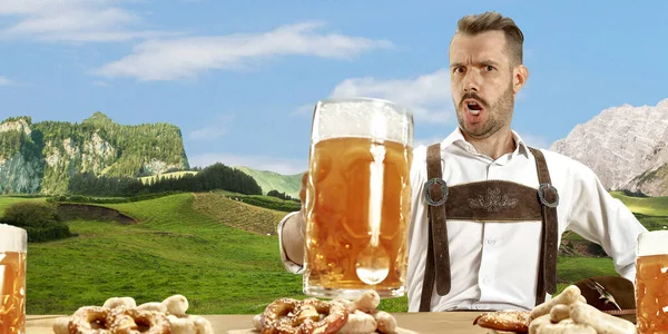 El hombre sonriente feliz con cerveza vestida con traje tradicional austriaco o bávaro sosteniendo taza de cerveza, montañas en el fondo, volante —  Fotos de Stock