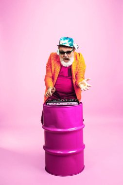Pembe arka planda poz veren gözlüklü kıdemli hippi. Teknolojik ve neşeli yaşlı yaşam tarzı konsepti