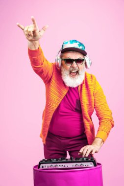 Pembe arka planda poz veren gözlüklü kıdemli hippi. Teknolojik ve neşeli yaşlı yaşam tarzı konsepti