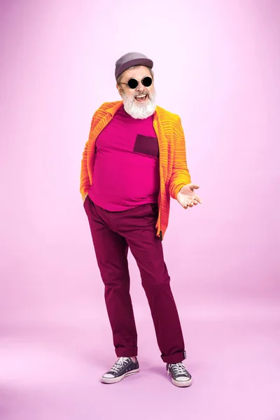 Senior hipster man wearing eyeglasses posing on pink background. Tech and joyful elderly lifestyle concept — Stock Photo, Image