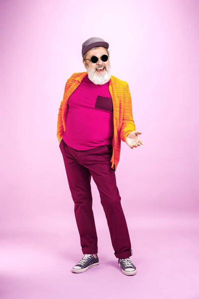 Senior hipster man wearing eyeglasses posing on pink background. Tech and joyful elderly lifestyle concept