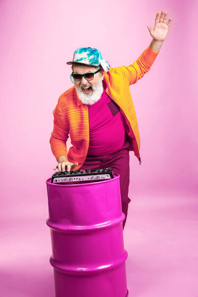 Senior hipster man wearing eyeglasses posing on pink background. Tech and joyful elderly lifestyle concept