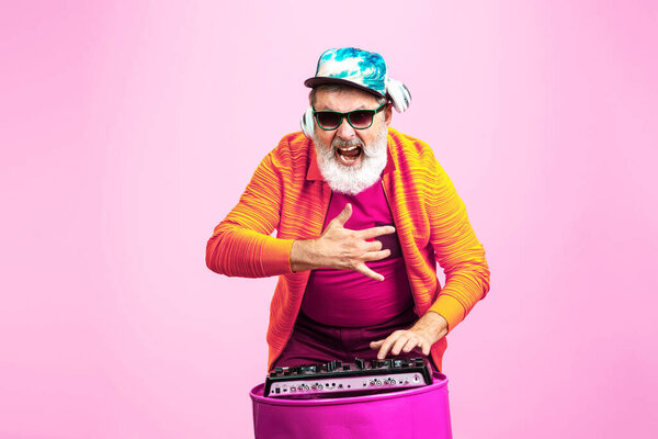 Senior hipster man wearing eyeglasses posing on pink background. Tech and joyful elderly lifestyle concept